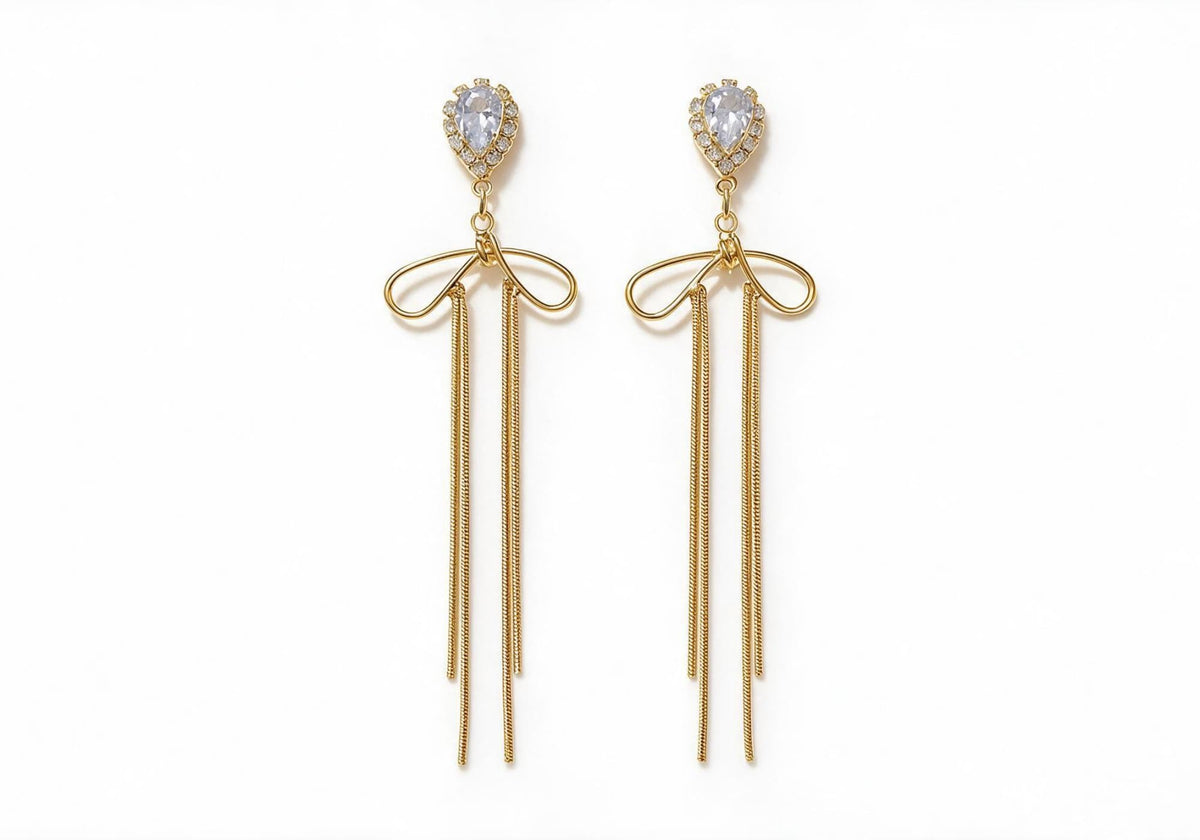 Gold-tone earrings featuring a teardrop center stone with a zircon halo, a metallic bow, and slender snake chain tassels.