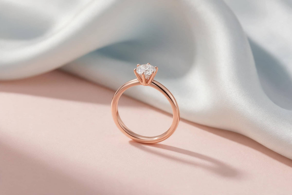MAROVA JEWELS timeless six-prong solitaire diamond ring in polished rose gold, minimalist engagement band design resting on smooth blush pink and ivory satin fabric, soft shadow, elegant luxury jewelry presentation