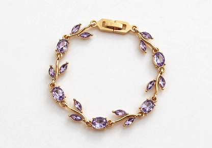 Gold-toned leaf vine bracelet with deep purple amethyst crystal stones on a beige velvet display box