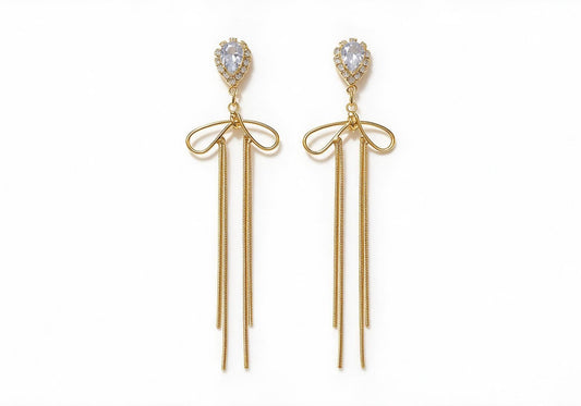 Gold-tone earrings featuring a teardrop center stone with a zircon halo, a metallic bow, and slender snake chain tassels.