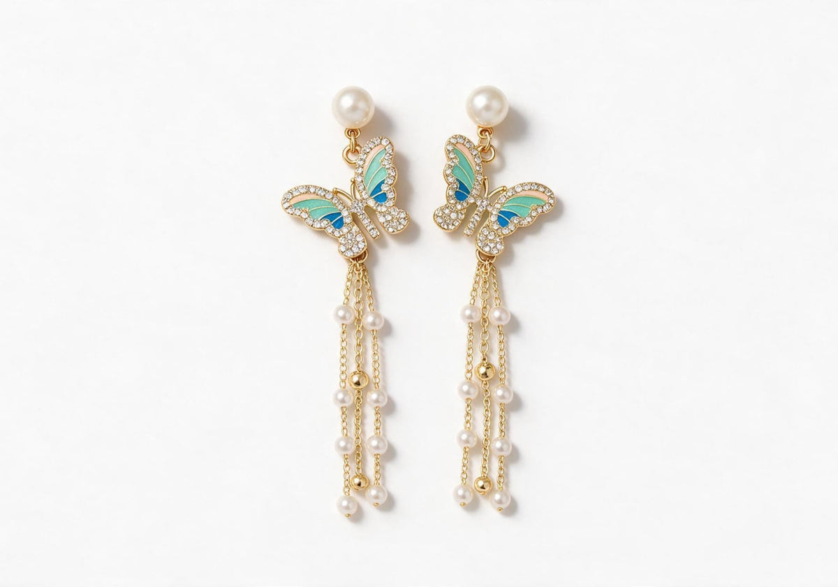 Gold-tone earrings featuring a faux pearl stud, a blue-green gradient enamel butterfly with pave edges, and cascading slender chains with faux pearls and gold beads.