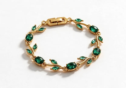Gold-toned leaf vine bracelet with emerald green crystal stones on a beige velvet display box
