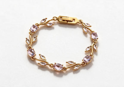Gold-toned leaf vine bracelet with light lavender purple crystal stones on a beige velvet display box