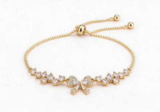 Gold box chain adjustable bracelet featuring a 3D bow made of pave zircon hearts with dangling baguette stones, fully paved with staggered round clear zirconia.