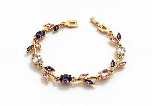 Gold-toned leaf vine bracelet with mixed purple, pink and clear crystal stones on a beige velvet display box